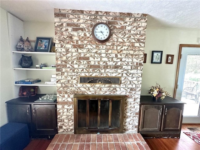 living area featuring visible vents, a fireplace, a textured ceiling, and wood finished floors