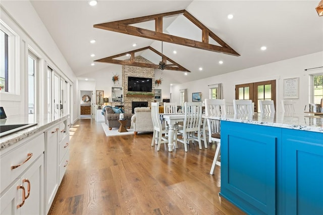 kitchen with ceiling fan, wood finished floors, white cabinetry, a brick fireplace, and light stone countertops