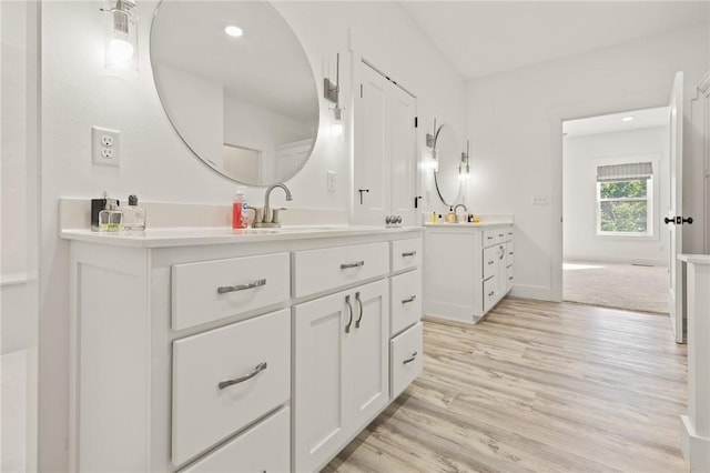 bathroom featuring wood finished floors, two vanities, a sink, and baseboards