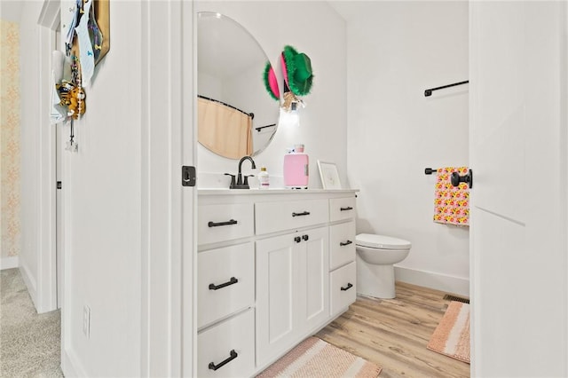 bathroom with visible vents, toilet, vanity, wood finished floors, and baseboards