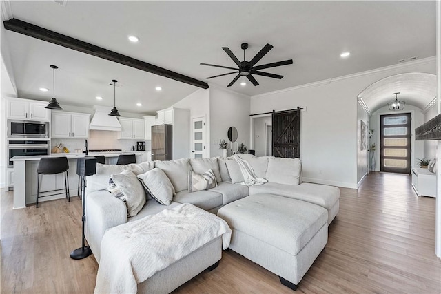 living area featuring lofted ceiling with beams, a barn door, light wood finished floors, and arched walkways