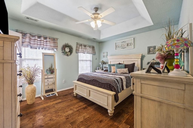 bedroom featuring baseboards, visible vents, a ceiling fan, dark wood-type flooring, and a tray ceiling