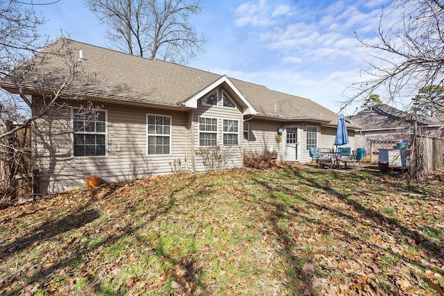 back of property with roof with shingles, fence, and a yard