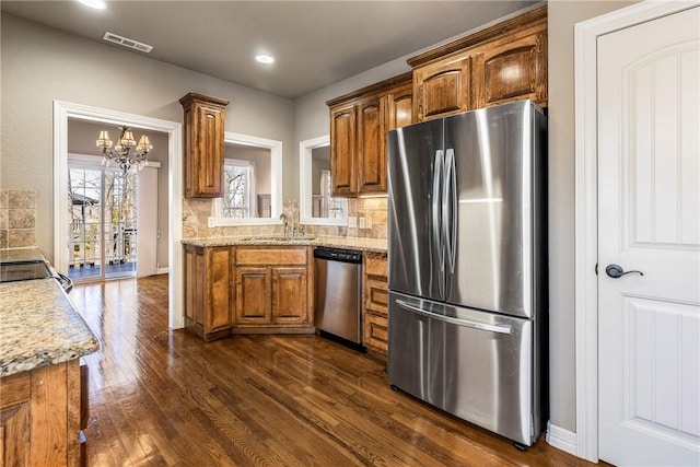 kitchen featuring stainless steel appliances, visible vents, brown cabinetry, dark wood-type flooring, and a sink