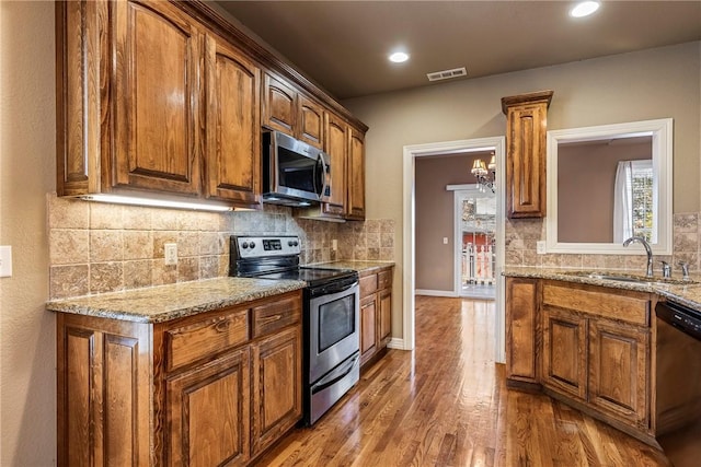 kitchen featuring brown cabinets, wood finished floors, a sink, stainless steel appliances, and backsplash