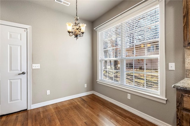 unfurnished dining area with a chandelier, visible vents, dark wood finished floors, and baseboards