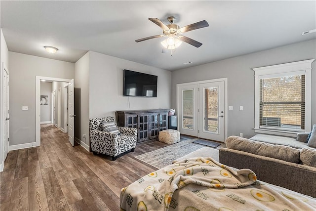 living area with a ceiling fan, wood finished floors, visible vents, and baseboards