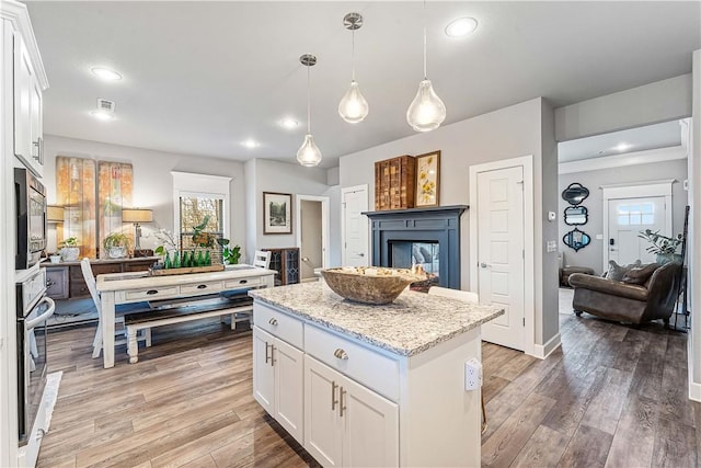 kitchen with stainless steel appliances, a kitchen island, light wood-style flooring, and a multi sided fireplace