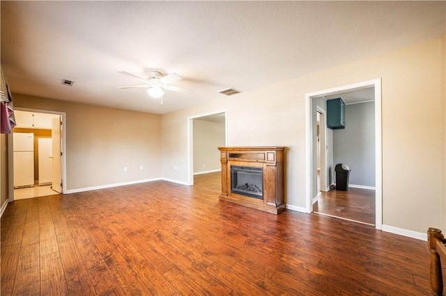 unfurnished living room featuring dark wood-style flooring, a fireplace, visible vents, and a ceiling fan