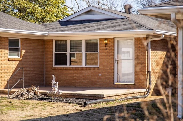 doorway to property with a shingled roof and brick siding