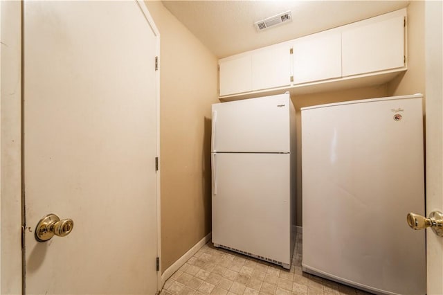 kitchen with baseboards, visible vents, white cabinets, freestanding refrigerator, and light floors