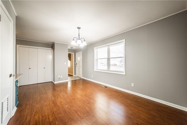 unfurnished bedroom with dark wood-style floors, visible vents, a closet, and an inviting chandelier