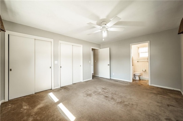 unfurnished bedroom with multiple closets, ensuite bathroom, carpet flooring, ceiling fan, and baseboards