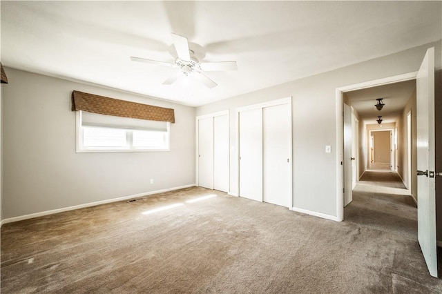 unfurnished bedroom featuring carpet flooring, ceiling fan, baseboards, and two closets