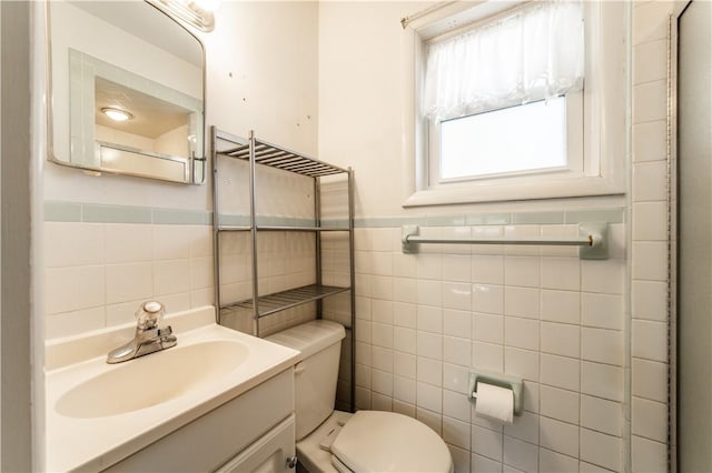 half bathroom featuring tile walls, wainscoting, vanity, and toilet