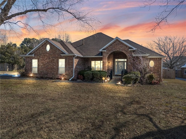 ranch-style house featuring a front yard, fence, brick siding, and roof with shingles