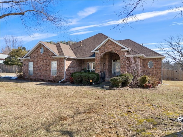 ranch-style house with a front yard, fence, brick siding, and roof with shingles