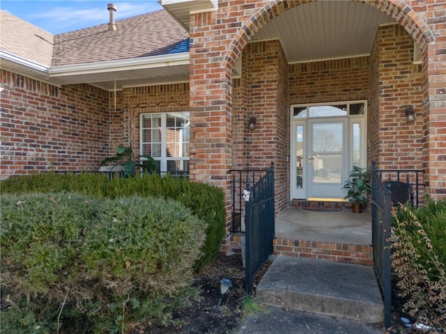 doorway to property featuring a shingled roof and brick siding