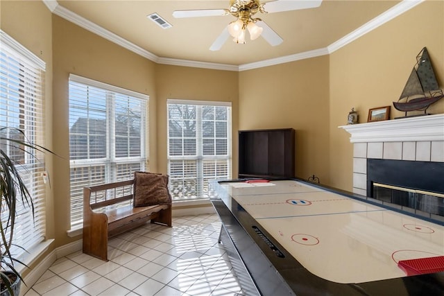 game room with visible vents, a tile fireplace, ceiling fan, crown molding, and light tile patterned flooring