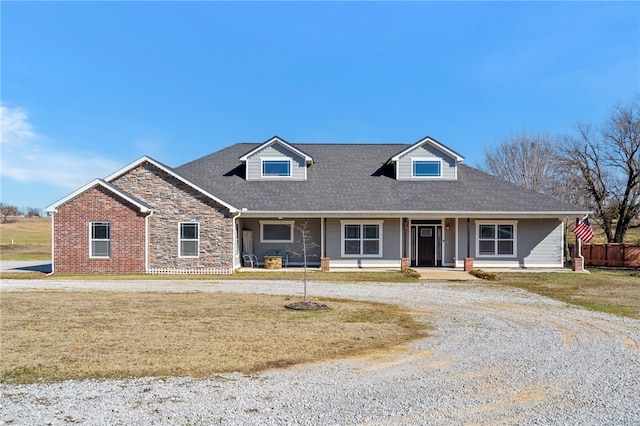 view of front of property featuring stone siding, covered porch, fence, and a front lawn