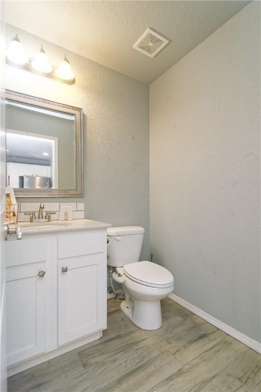 bathroom with visible vents, a textured wall, toilet, vanity, and wood finished floors