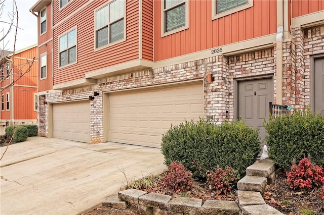 property entrance with driveway, brick siding, board and batten siding, and an attached garage