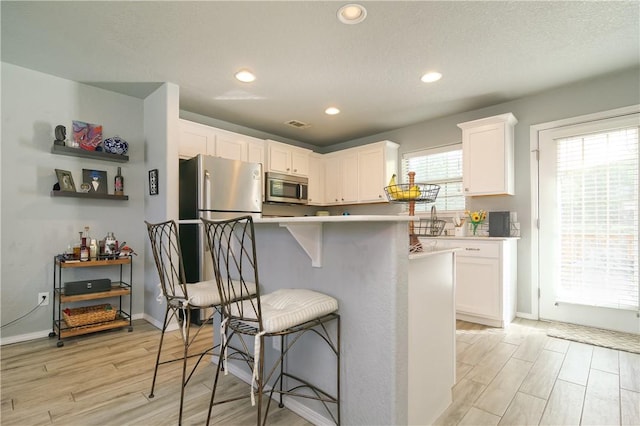 kitchen with stainless steel microwave, a kitchen breakfast bar, light countertops, light wood-type flooring, and white cabinetry