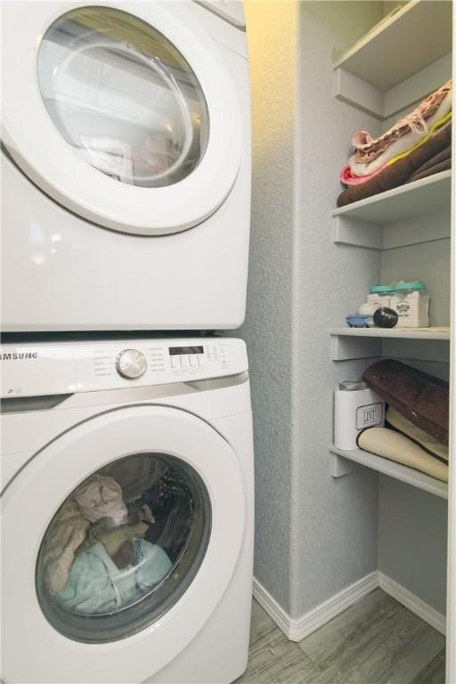 clothes washing area with baseboards, laundry area, wood finished floors, and stacked washer / drying machine