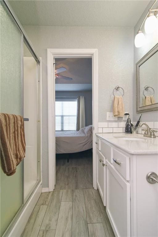 ensuite bathroom featuring wood finish floors, vanity, a ceiling fan, a stall shower, and ensuite bath