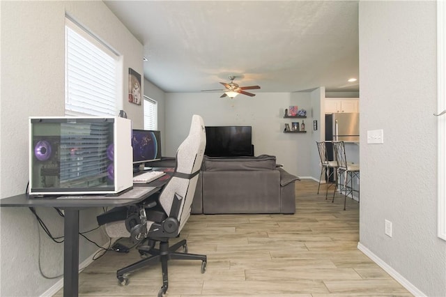 office area featuring light wood-style floors, baseboards, a ceiling fan, and a textured wall