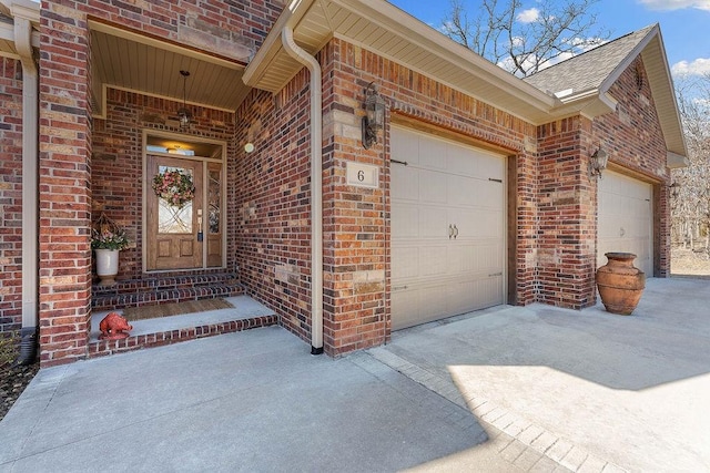 property entrance featuring a garage, concrete driveway, brick siding, and roof with shingles