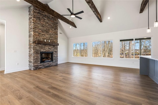 unfurnished living room with ceiling fan, a fireplace, wood finished floors, baseboards, and beamed ceiling