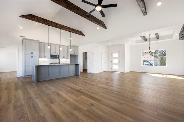 kitchen featuring stainless steel microwave, wood finished floors, gray cabinets, beam ceiling, and ceiling fan with notable chandelier