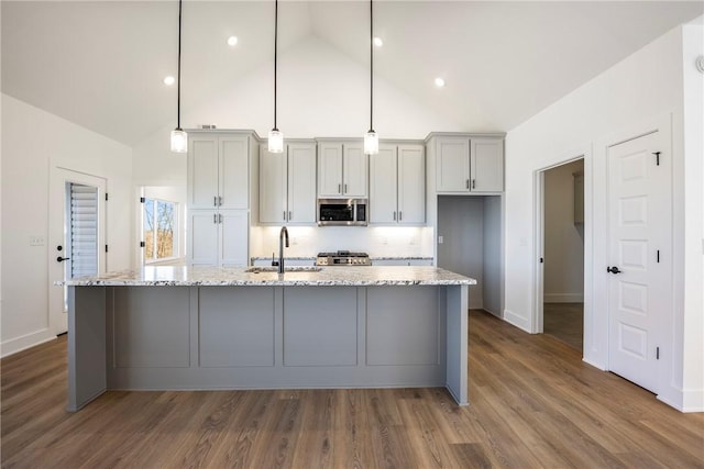 kitchen featuring dark wood finished floors, stainless steel microwave, stove, a kitchen island with sink, and a sink