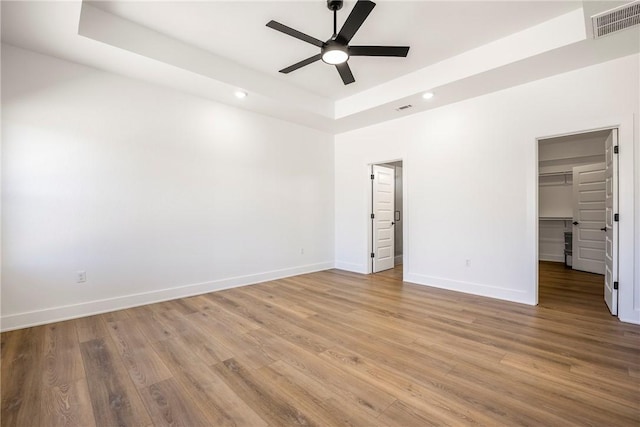 unfurnished bedroom featuring visible vents, baseboards, a spacious closet, light wood-type flooring, and a raised ceiling