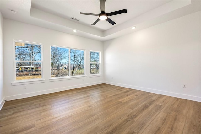 spare room featuring a tray ceiling, wood finished floors, visible vents, and baseboards