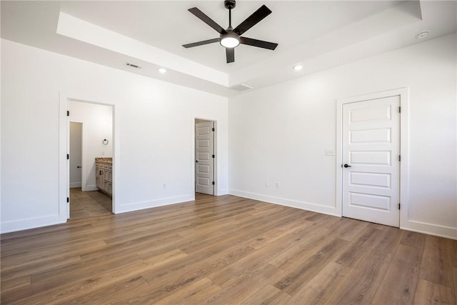 unfurnished bedroom with baseboards, a raised ceiling, and light wood-style floors