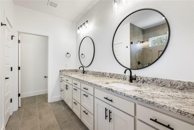 bathroom featuring a tile shower, double vanity, a sink, and visible vents