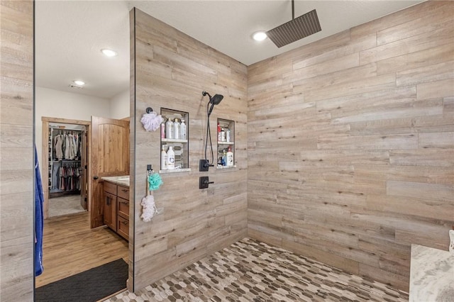 full bathroom with wood walls, a tile shower, vanity, and wood finished floors