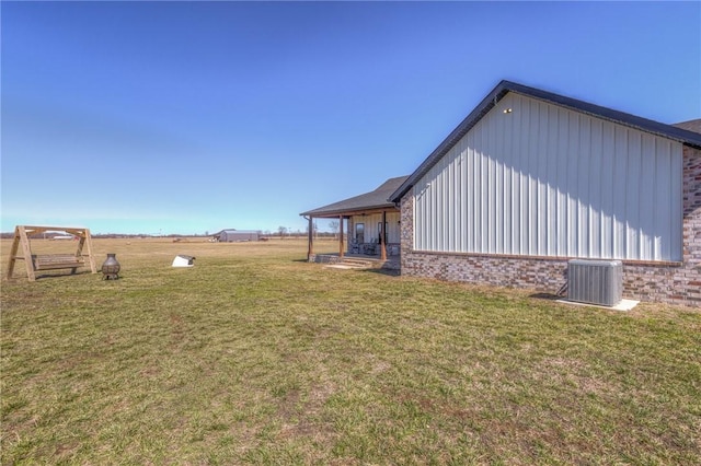 view of side of property with a yard, brick siding, and central AC