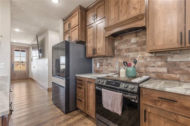 kitchen with light wood-style floors, brown cabinets, custom exhaust hood, and stainless steel electric range