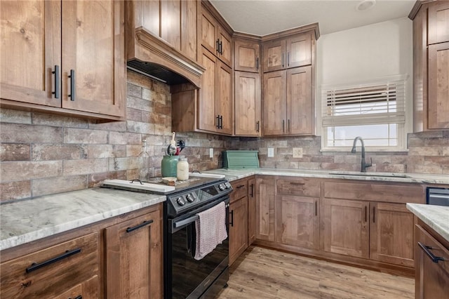 kitchen featuring tasteful backsplash, light wood-type flooring, custom exhaust hood, black electric range, and a sink