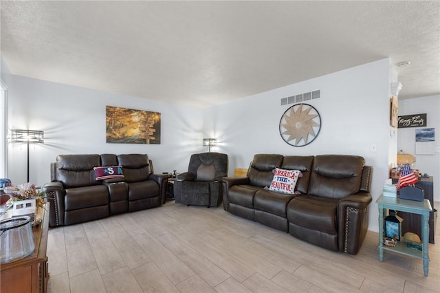 living area with light wood-type flooring, visible vents, and a textured ceiling