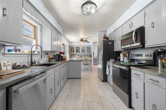 kitchen featuring light wood finished floors, stainless steel appliances, white cabinets, a sink, and ceiling fan