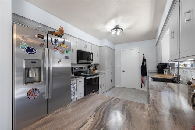 kitchen featuring light wood finished floors, white cabinets, appliances with stainless steel finishes, light countertops, and a sink