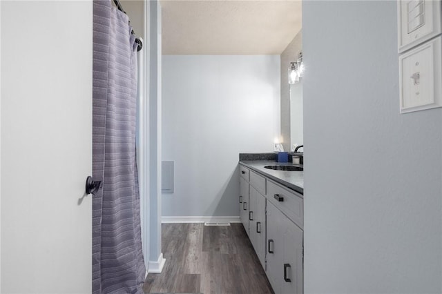 full bath with a shower with shower curtain, wood finished floors, vanity, and baseboards