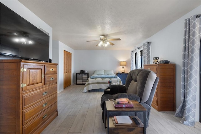 bedroom featuring a textured ceiling, a closet, a ceiling fan, and light wood-style floors