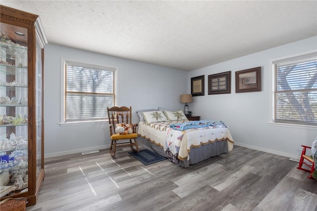 bedroom with a textured ceiling, baseboards, and wood finished floors