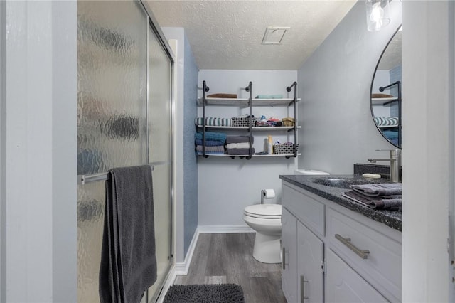 bathroom featuring wood finished floors, toilet, vanity, a shower stall, and a textured ceiling