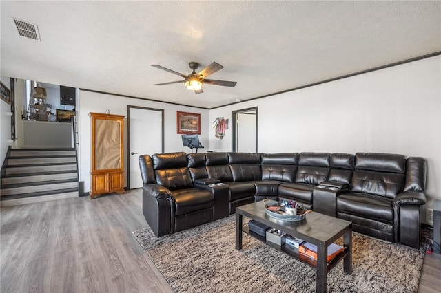 living room with ceiling fan, a textured ceiling, wood finished floors, visible vents, and stairs